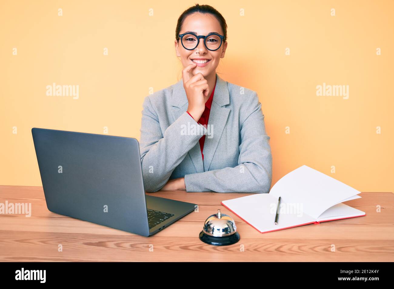 Young brunette woman working at hotel reception using laptop smiling ...