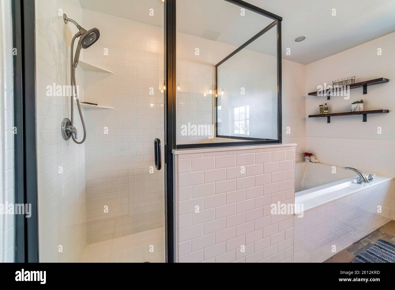 Glass shower stall and built in bathtub inside bathroom with white and