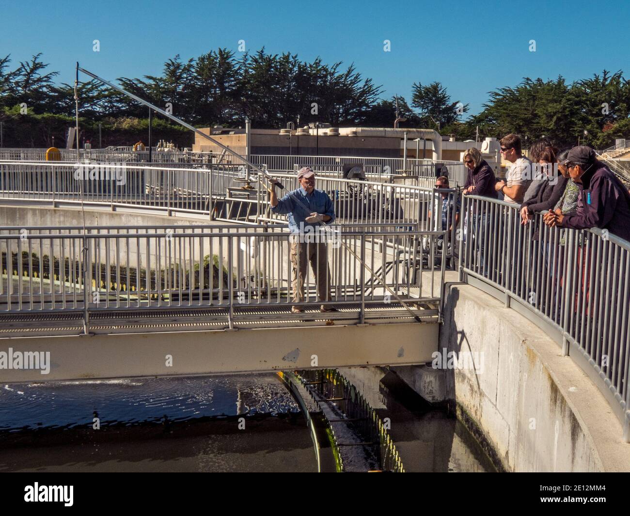 Waste water treatment plant operator explains a technique for measuring the depth of activated sludge in the bottom of a wastewater clarifier. Stock Photo