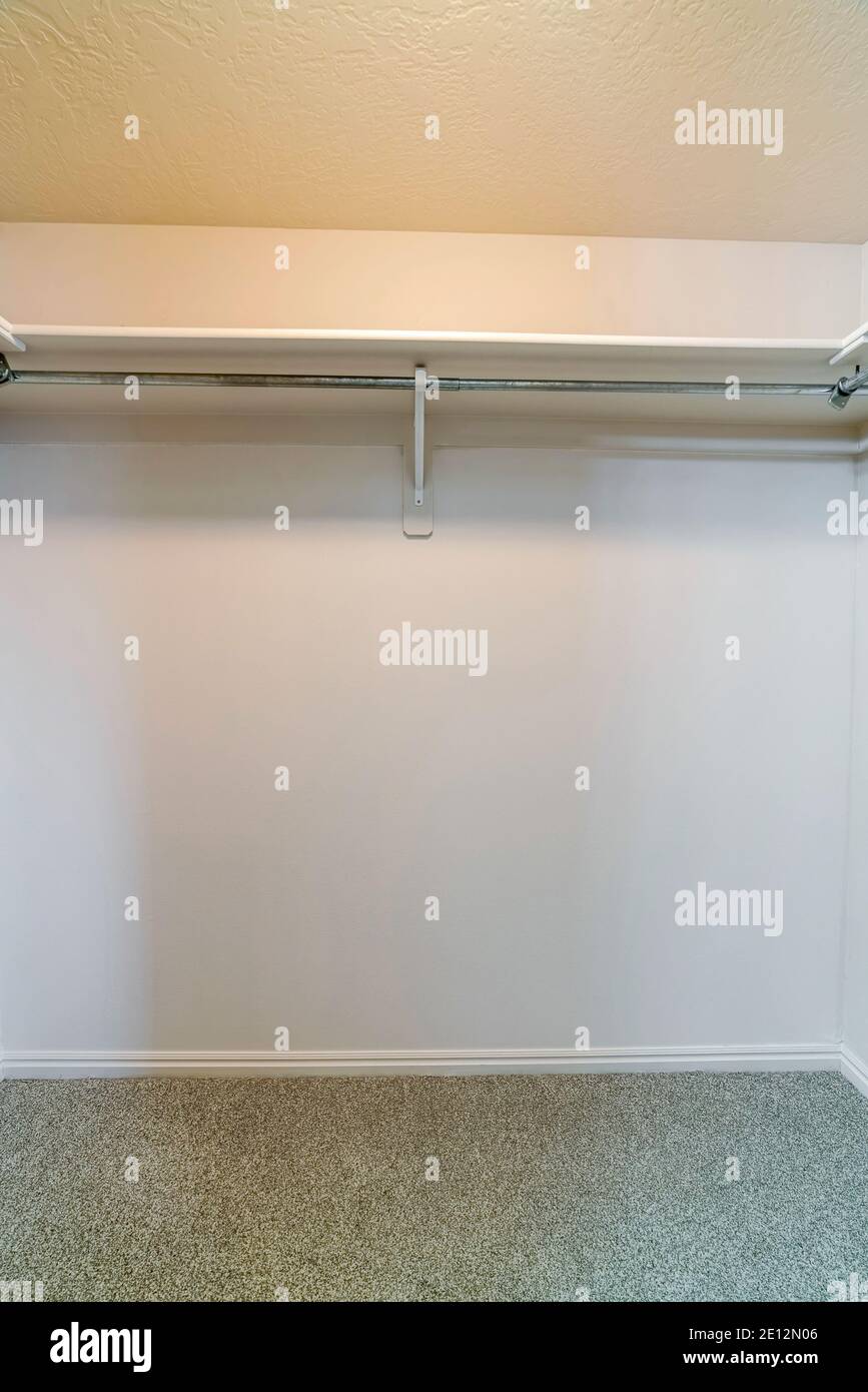 Wooden built in shelf with clothes rod mounted on white wall of a