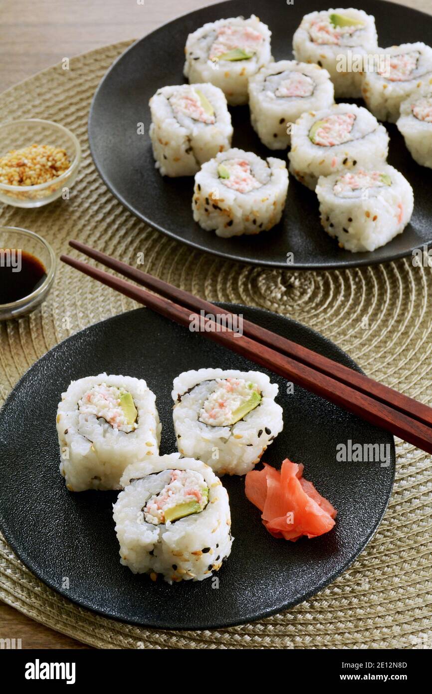 Fresh made California sushi rolls on black plates in vertical format. Red ginger slices, sesame
