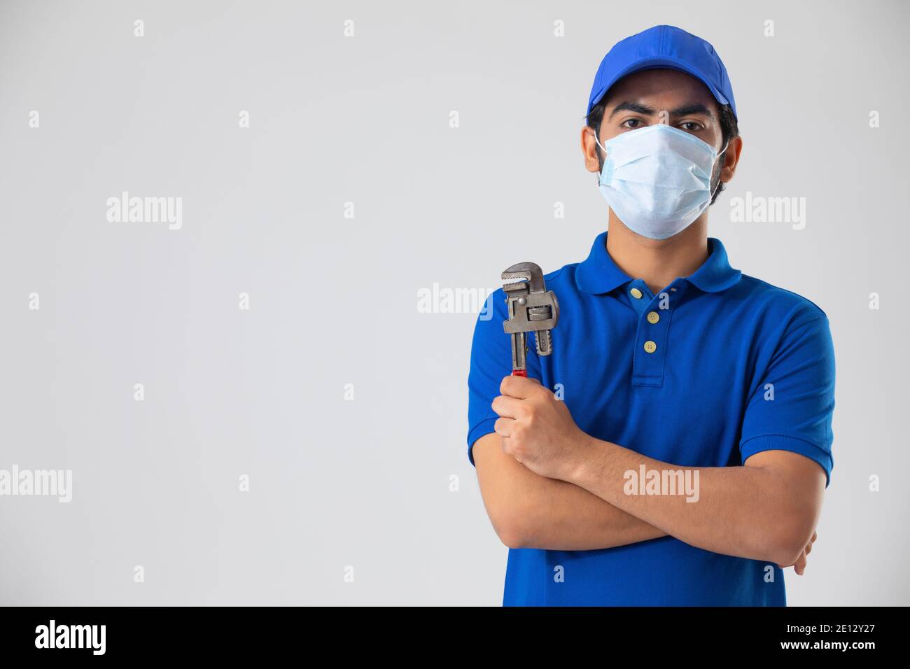 A PLUMBER WEARING FACE MASK HOLDING TOOL AND LOOKING AT CAMERA Stock Photo