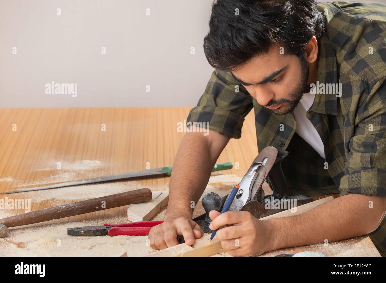 A YOUNG CARPENTER MEASURING WOOD WHILE WORKING Stock Photo