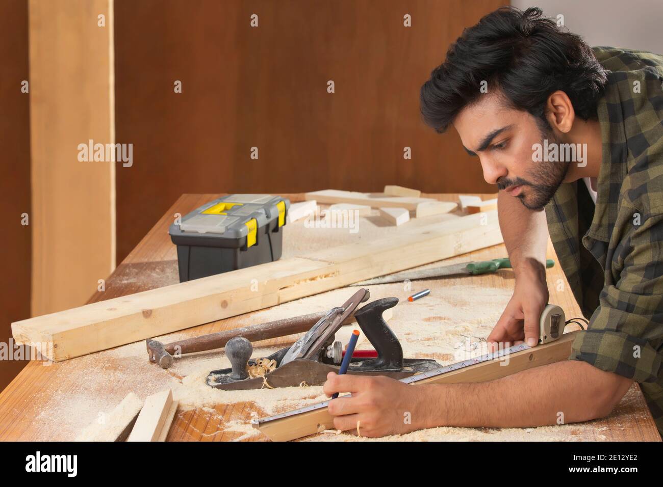 A YOUNG CARPENTER CAREFULLY MEASURING WOOD AND WORKING Stock Photo
