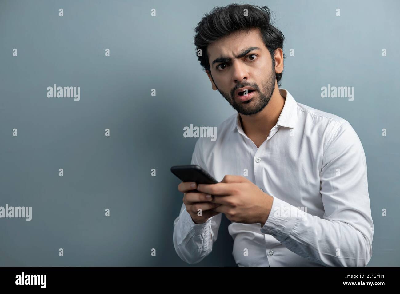 A YOUNG EXECUTIVE LOOKING AT CAMERA AND FEELING SURPRISED WHILE USING MOBILE PHONE Stock Photo