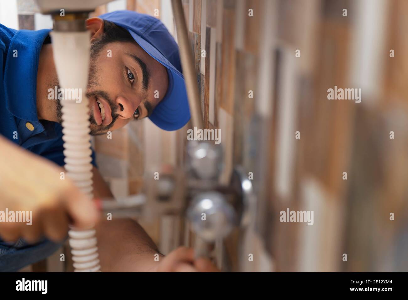 A PLUMBER LEANING DOWN AND FIXING PIPE Stock Photo