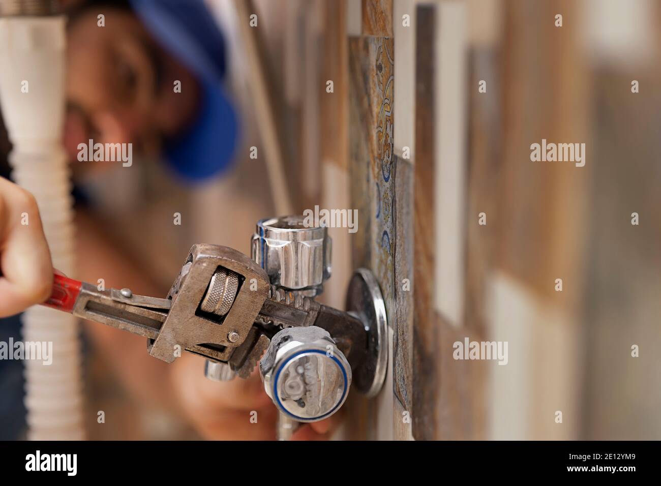 A LEAKING PIPE BEING FIXED BY A PLUMBER IN BACKGROUND Stock Photo