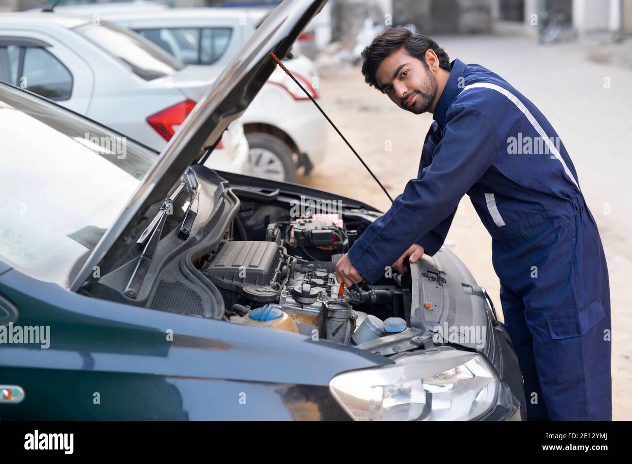 A YOUNG MECHANIC LOOKING AT CAMERA WHILE REPAIRING A CAR Stock Photo