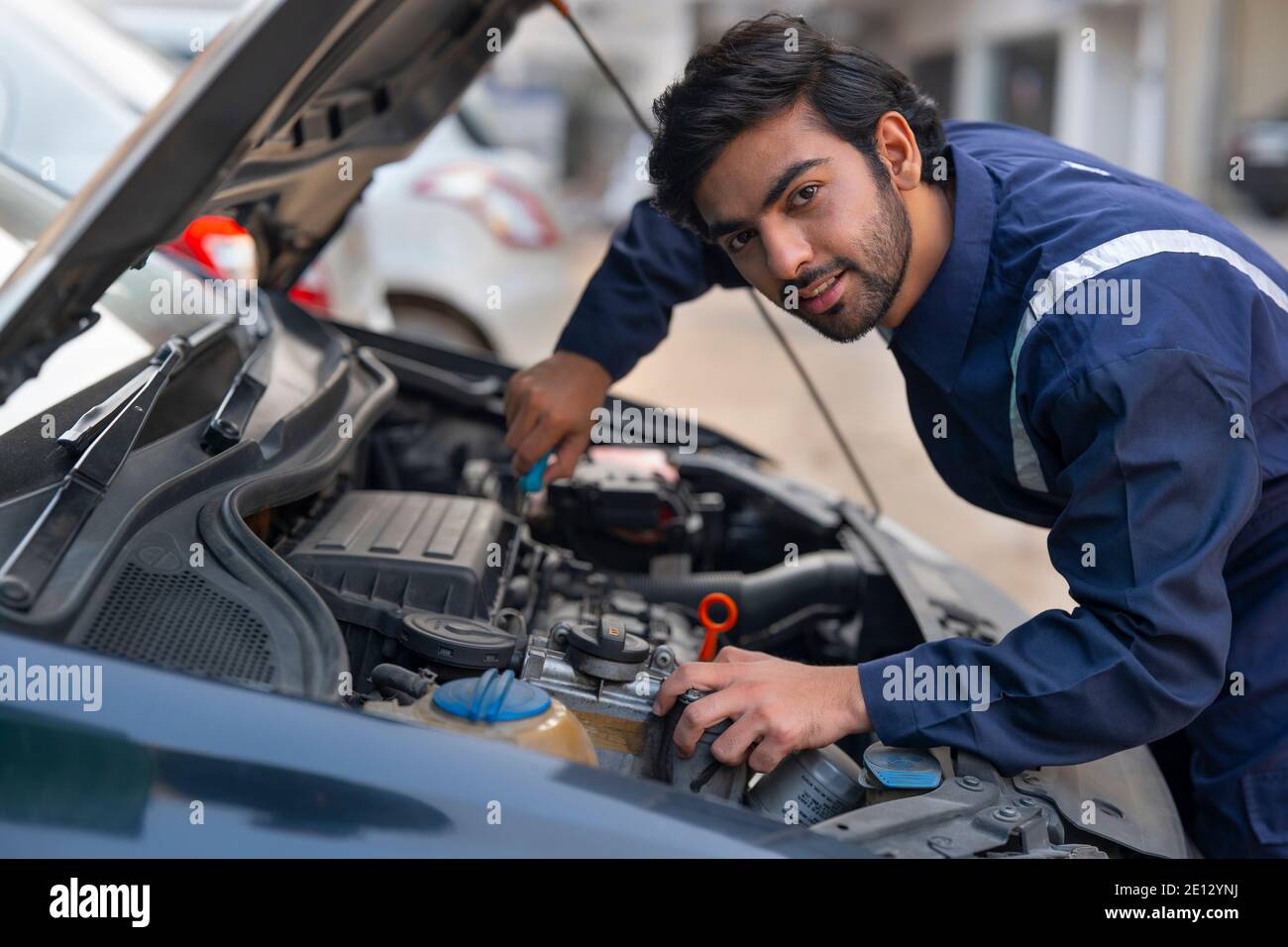 A MECHANIC REPAIRING A CAR AND LOOKING STRAIGHT Stock Photo