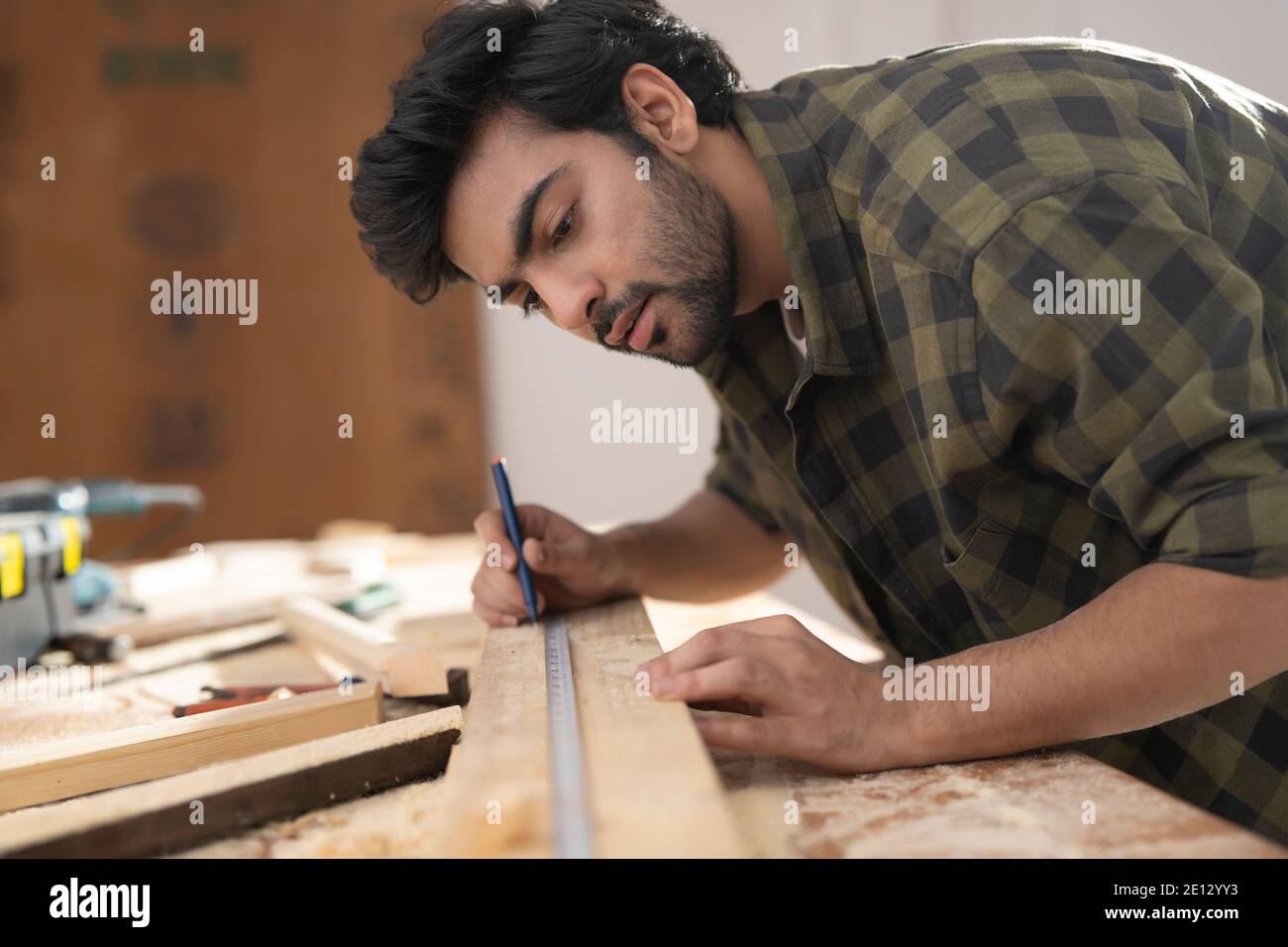 A YOUNG CARPENTER MARKING WOOD USING SCALE WHILE WORKING Stock Photo