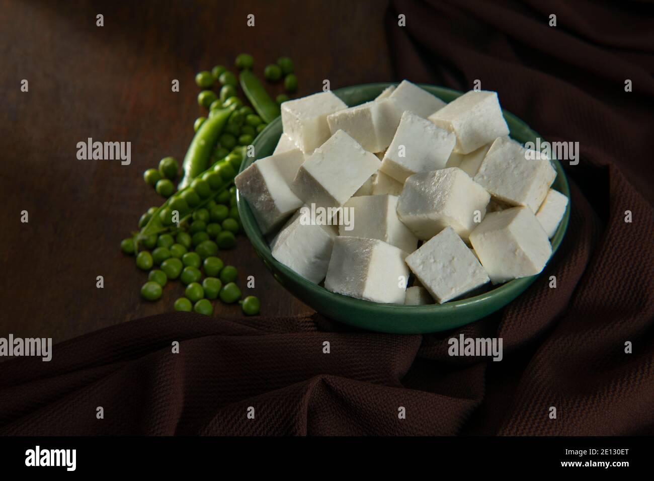 Diced Paneer in a green bowl with fresh raw peas Stock Photo