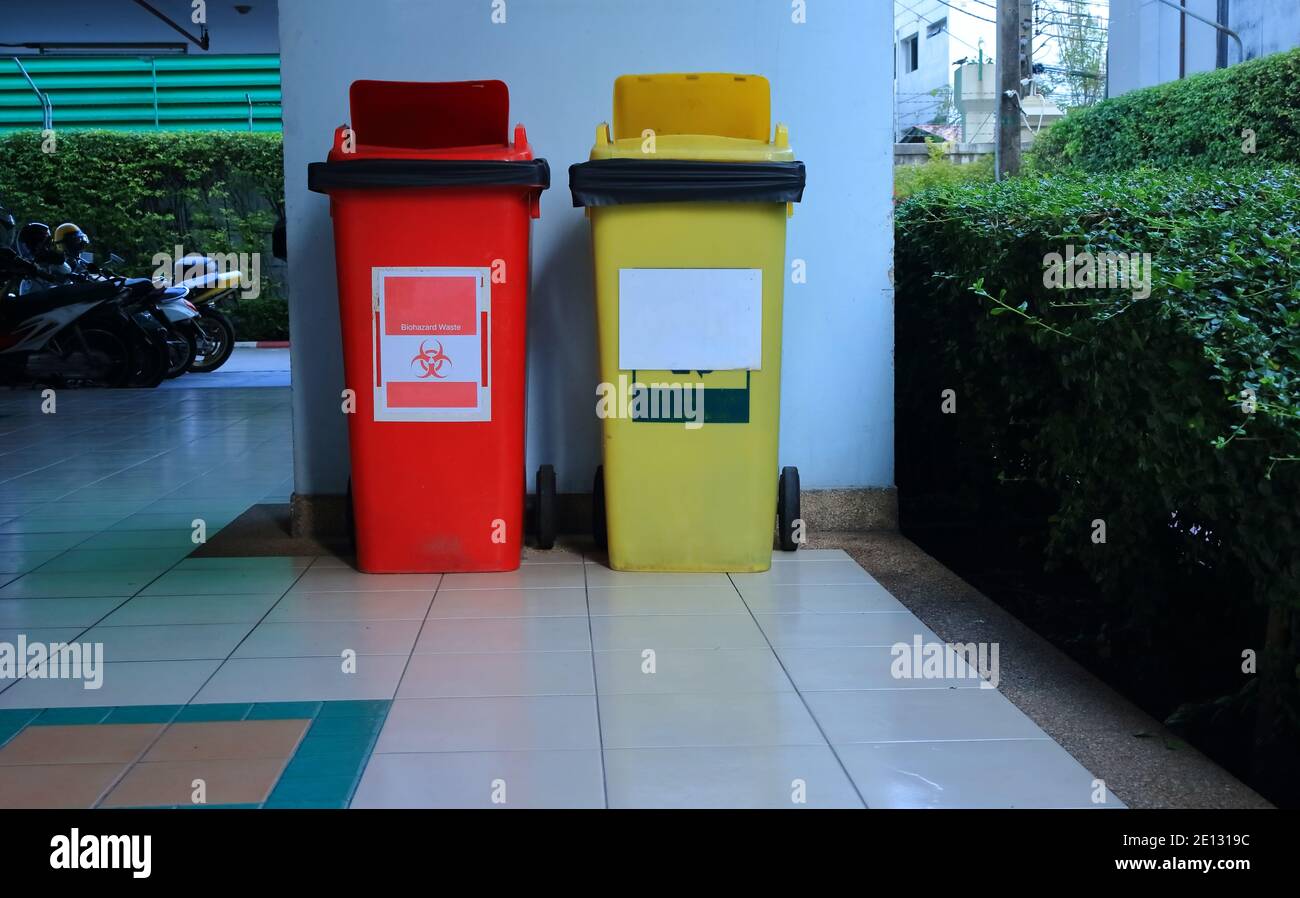 Closeup red biohazard bin standing on tiled floor next to yellow recycling bin against blue wall in a building Stock Photo