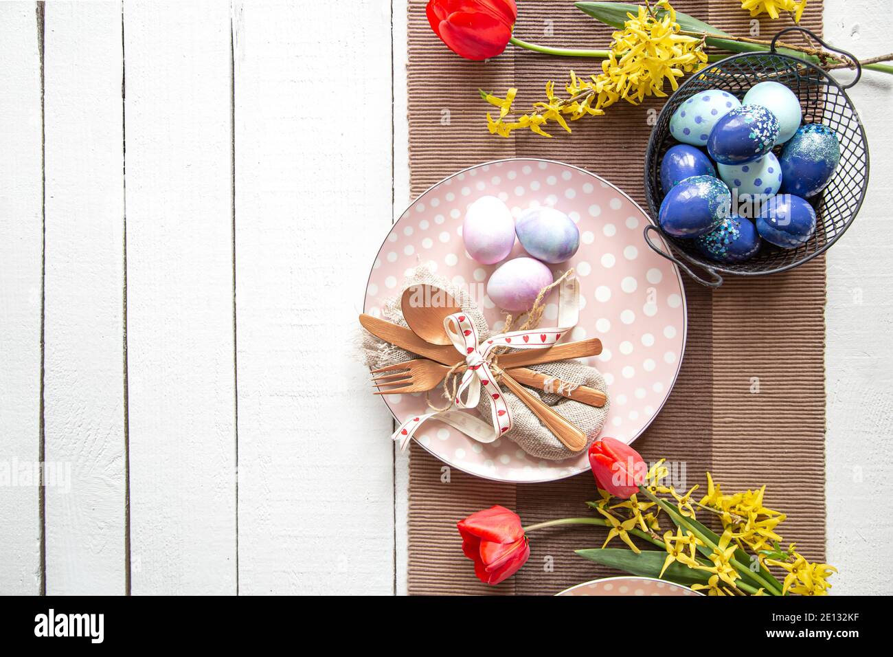 Plates with Easter cake, flowers and Easter eggs. Table setting for the Easter holiday copy space. Stock Photo