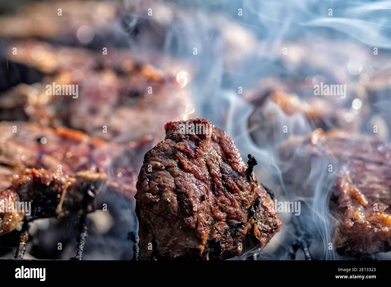 Meat on skewers grilled over an open fire with smoke close up. Barbecue