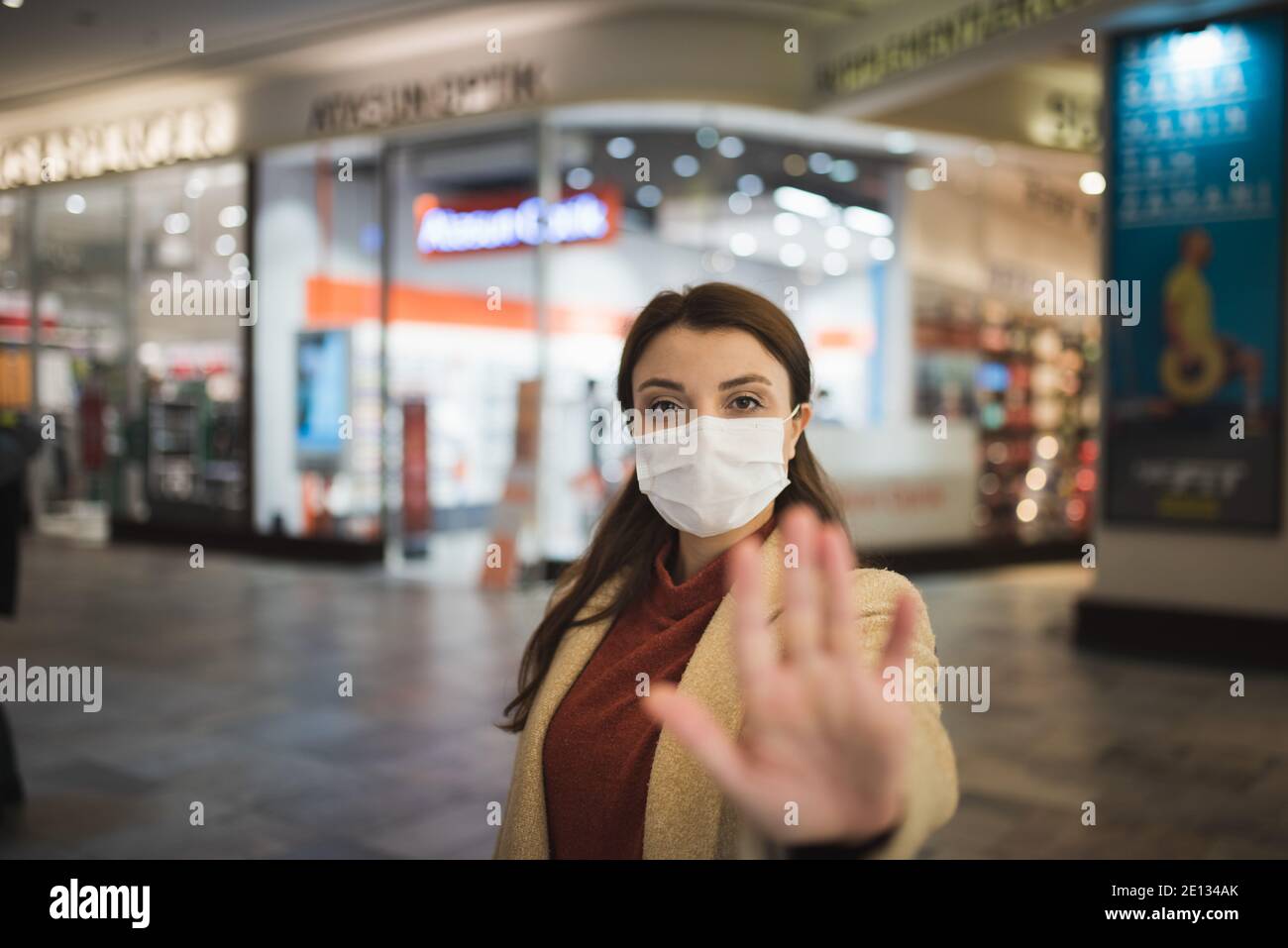 Beautiful girl wearing protective medical mask and fashionable clothes holds hand up as stop sign New normal lifestyle concept. Stock Photo