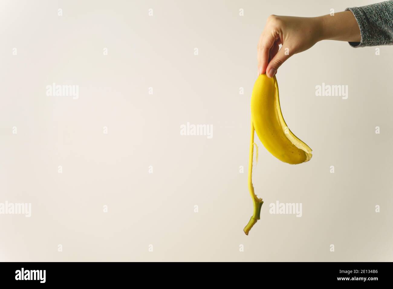 Hand of unknown caucasian woman holding banana peel in front of white wall - copy space concept of ending and finish trash ready to be thrown away old Stock Photo