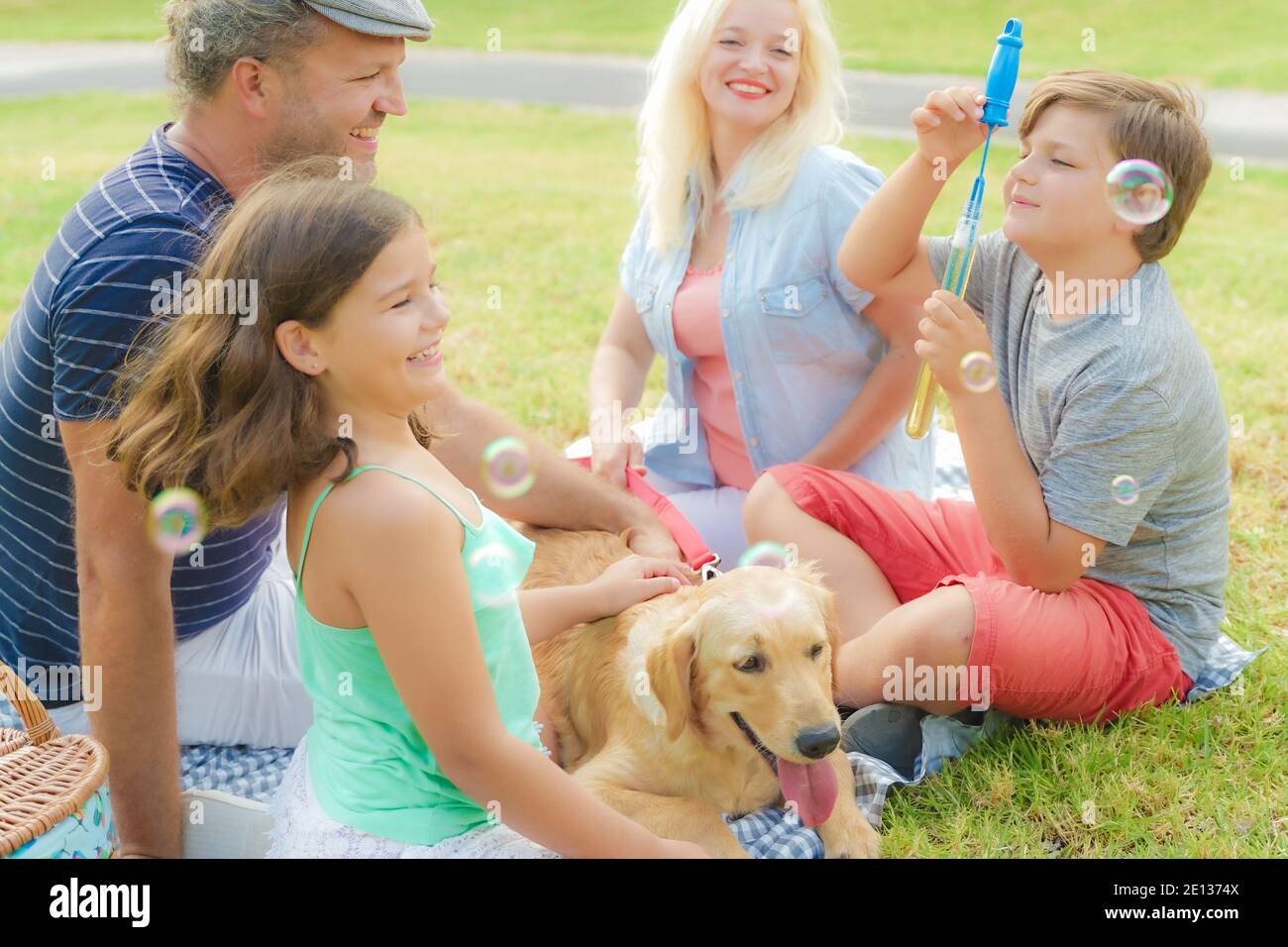 Happy family with their dog in a beautiful weekend. The boy playing with soap bubbles. Happy family going picnic in the park . Travel, pet,  holiday a Stock Photo