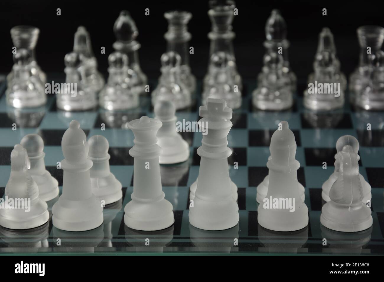 Clear glass chess pieces on a glass chessboard isolated on a black ...
