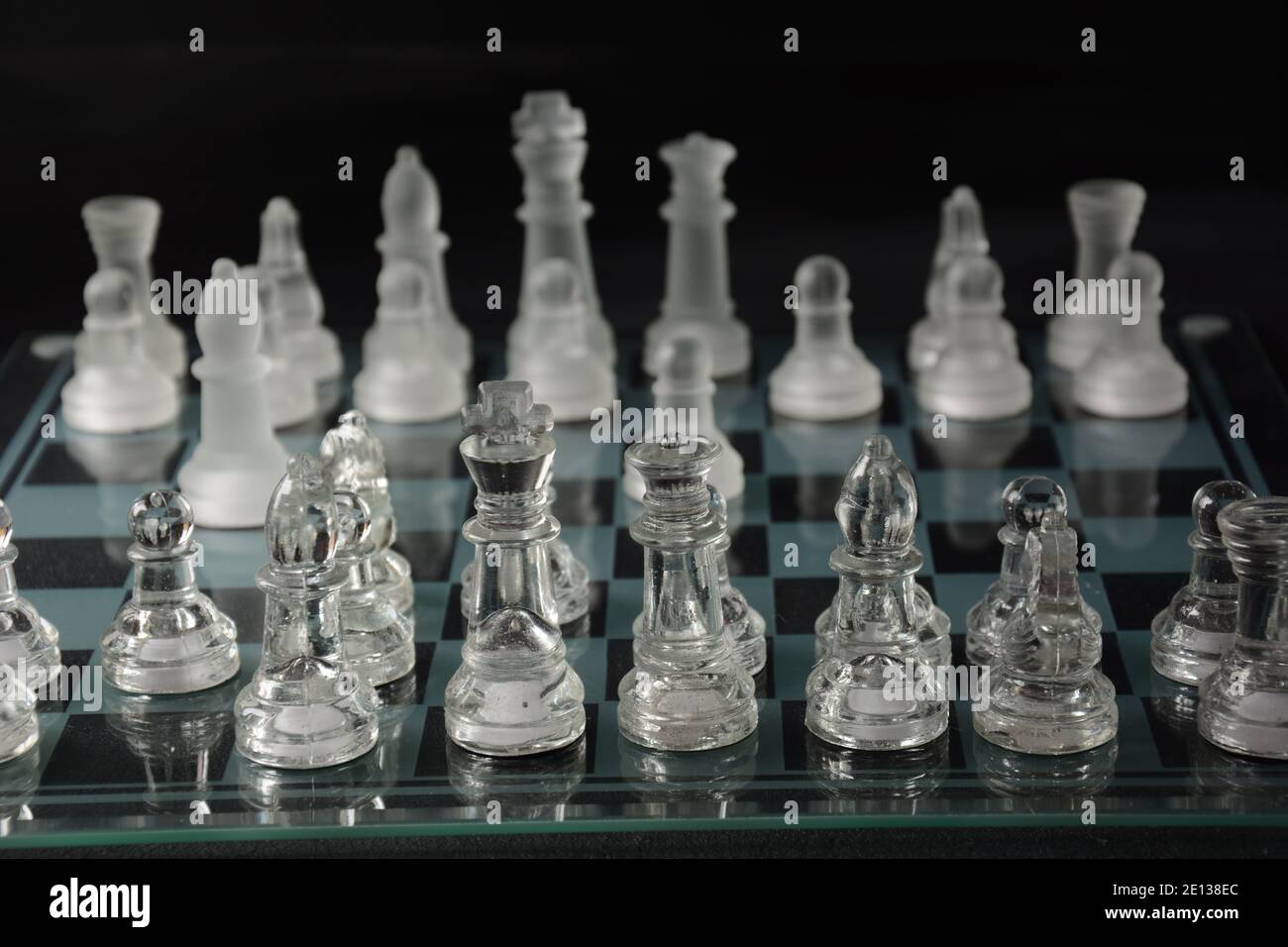 Clear glass chess pieces on a glass chessboard isolated on a black ...