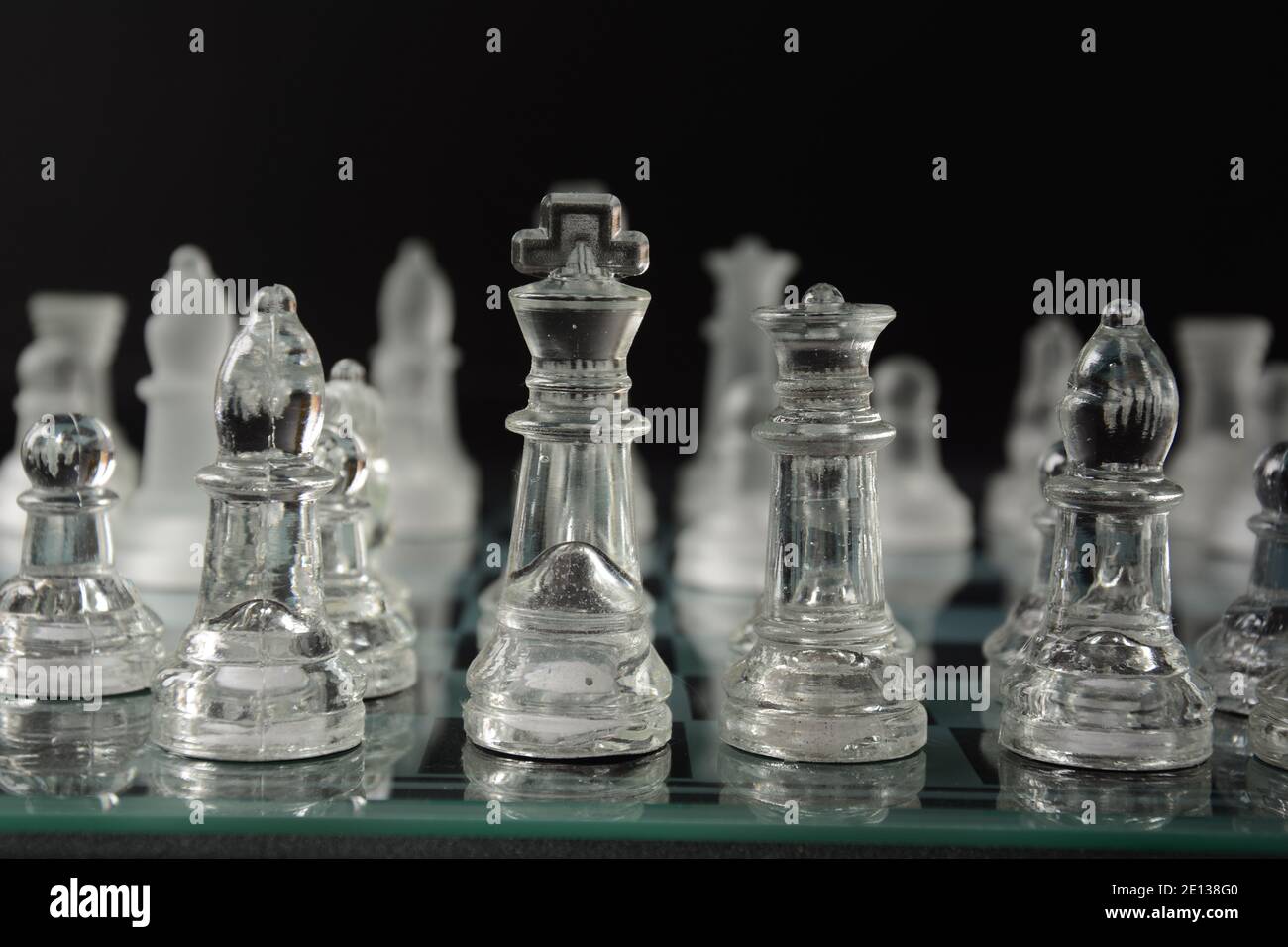 Clear glass chess pieces on a glass chessboard isolated on a black ...