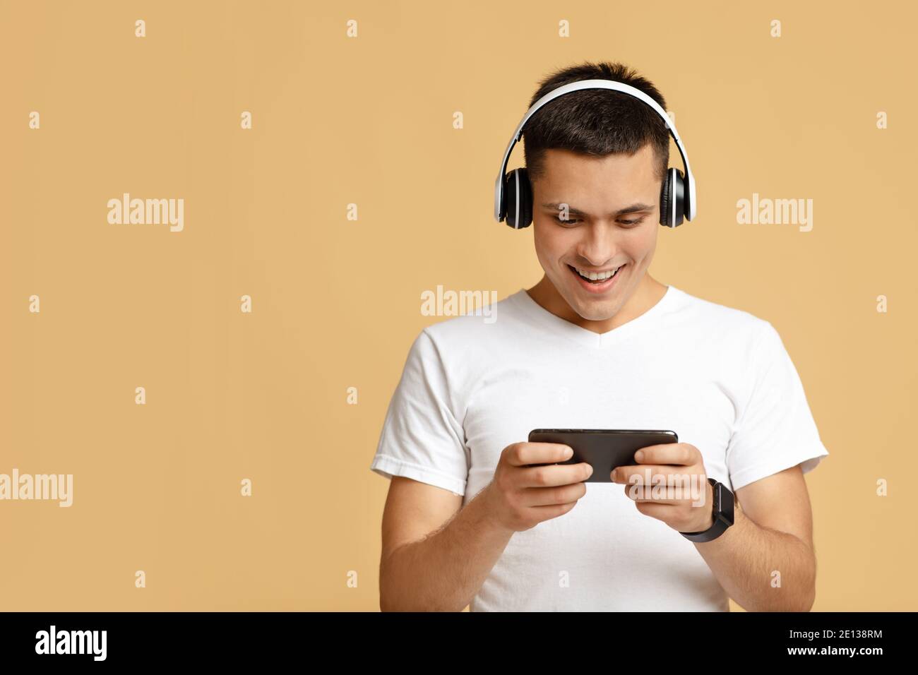 Entertainment and online games for teenagers. Cheerful cute millennial guy in modern wireless headphones Stock Photo