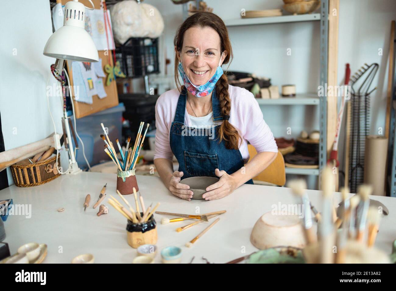 Happy artist woman molding with clay at pottery workshop - Focus on face Stock Photo