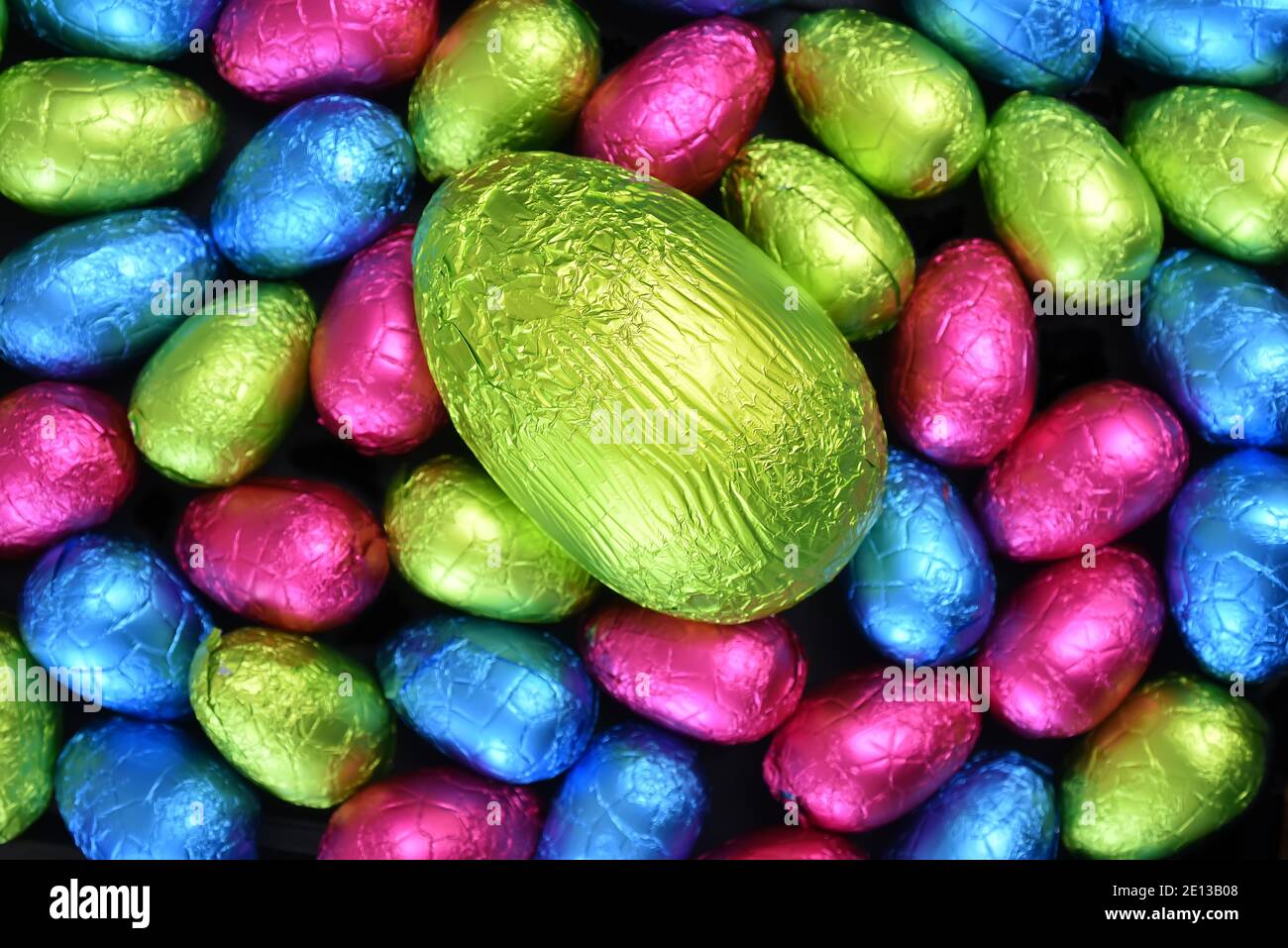 Pile group of multi coloured, different sizes of colourful foil wrapped chocolate easter eggs in pink, blue, yellow and lime green with a large egg. Stock Photo