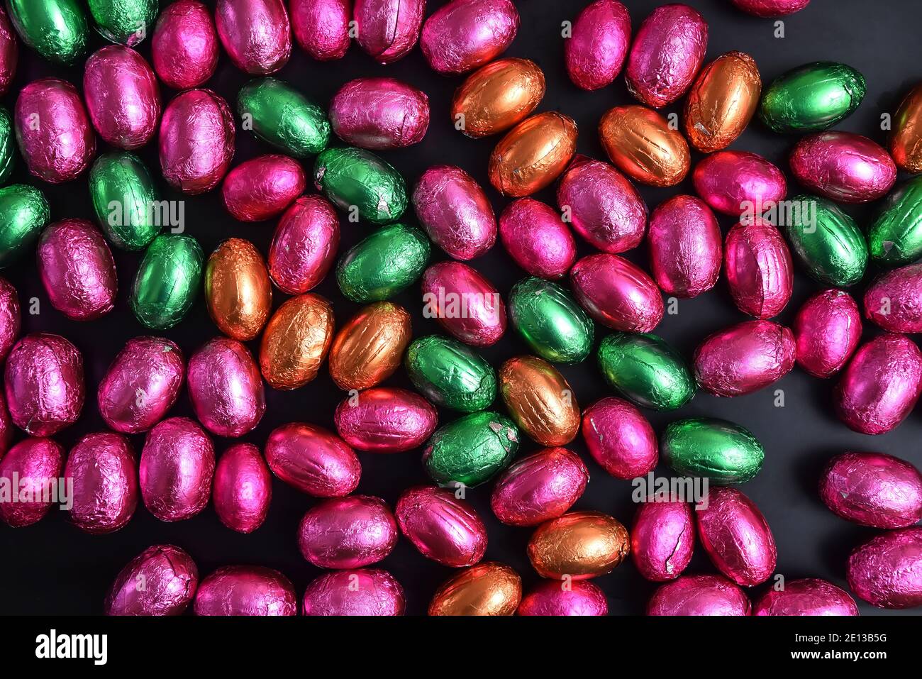Pink, green, orange and bronze foil wrapped chocolate easter eggs, against a black background. Stock Photo