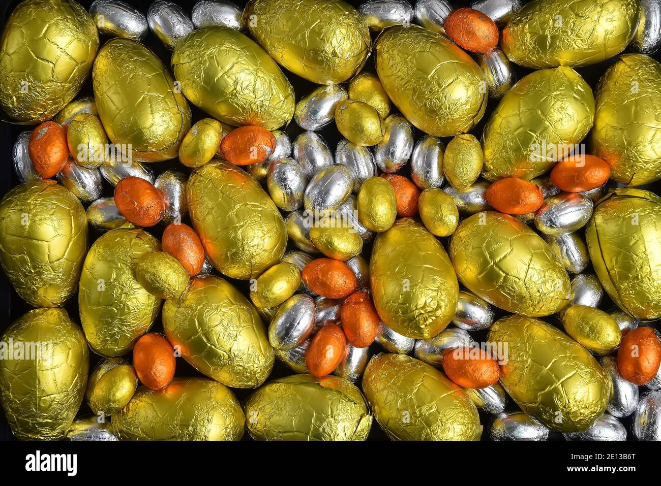Large & small yellow, gold, orange and silver spring colours of foil wrapped chocolate easter eggs, against a black background. Stock Photo