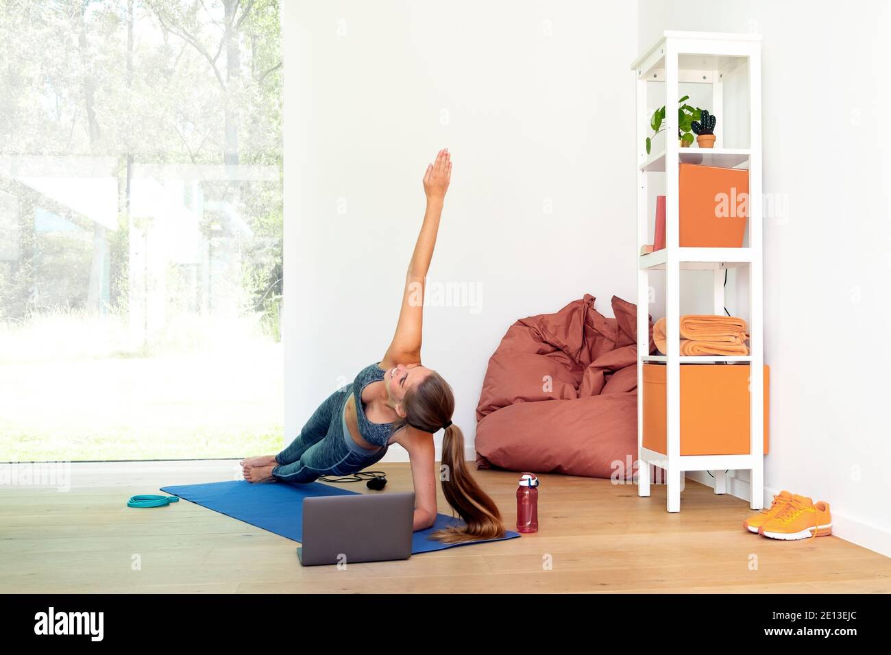 young sporty woman at home doing sports exercises using a laptop. Girl lying on the mat following online sports tutorial. Stock Photo