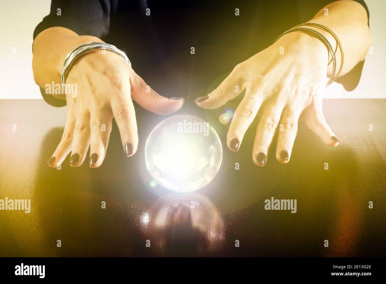 Fortune teller or soothsayer with a glowing crystal ball or sphere reflected on a shiny wooden table in a close up view of her hands Stock Photo