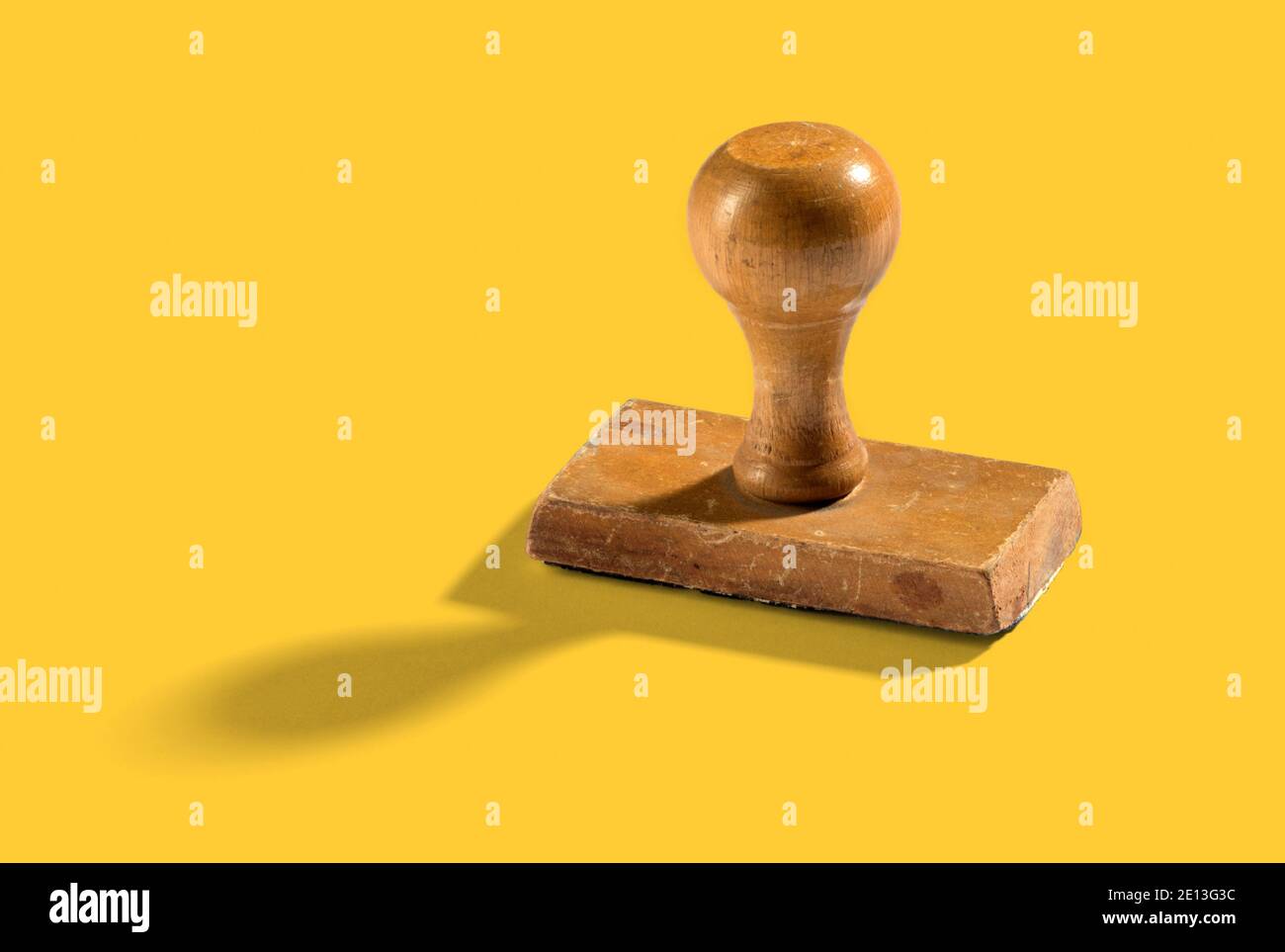 Wooden vintage hand stamp standing upright on yellow background with a shadow and copy space alongside Stock Photo