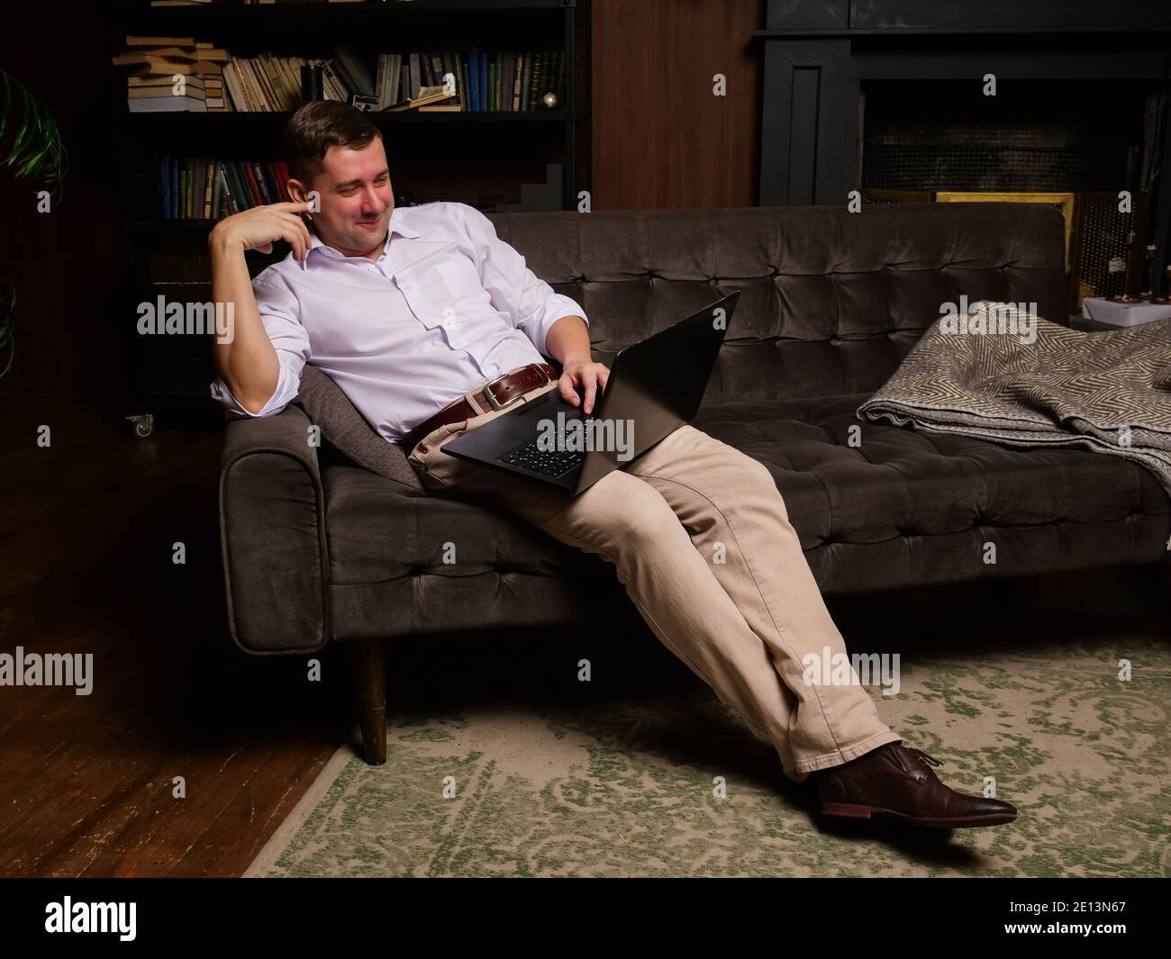Smiling man watching video on laptop or chatting online while sitting on the couch at home. Stock Photo