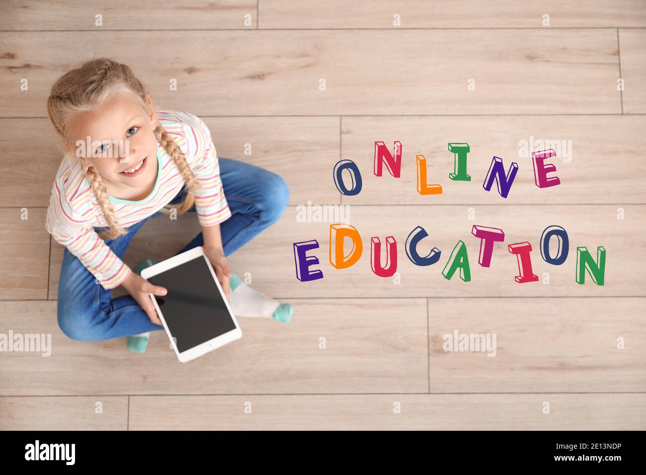 Text 'Online Education' and cute little girl with tablet computer learning at home Stock Photo