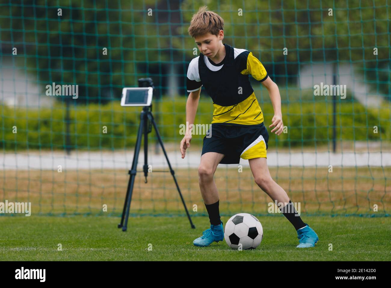 New technology on soccer training. Teenager running with football ball. Tablet on a stand in the background. Youth soccer team training unit Stock Photo