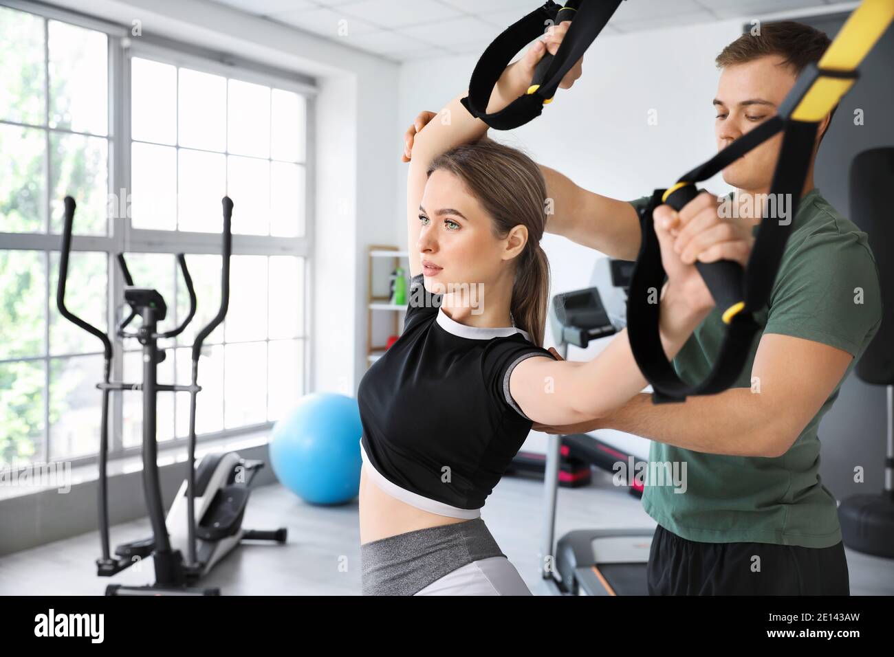 Coach helping young woman to train with TRX straps in gym Stock Photo -  Alamy