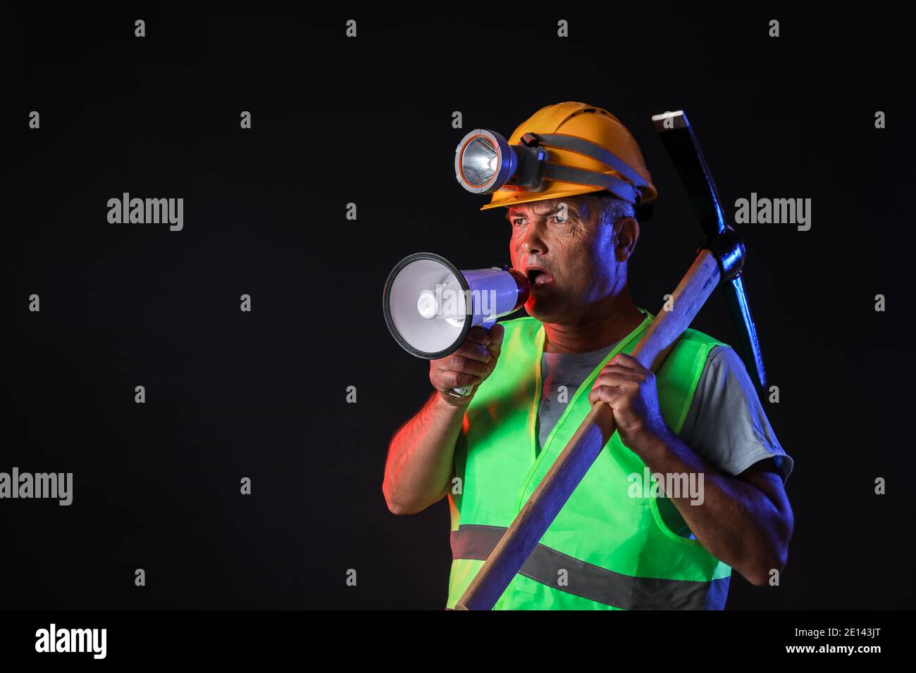 Protesting miner man with megaphone on dark background Stock Photo