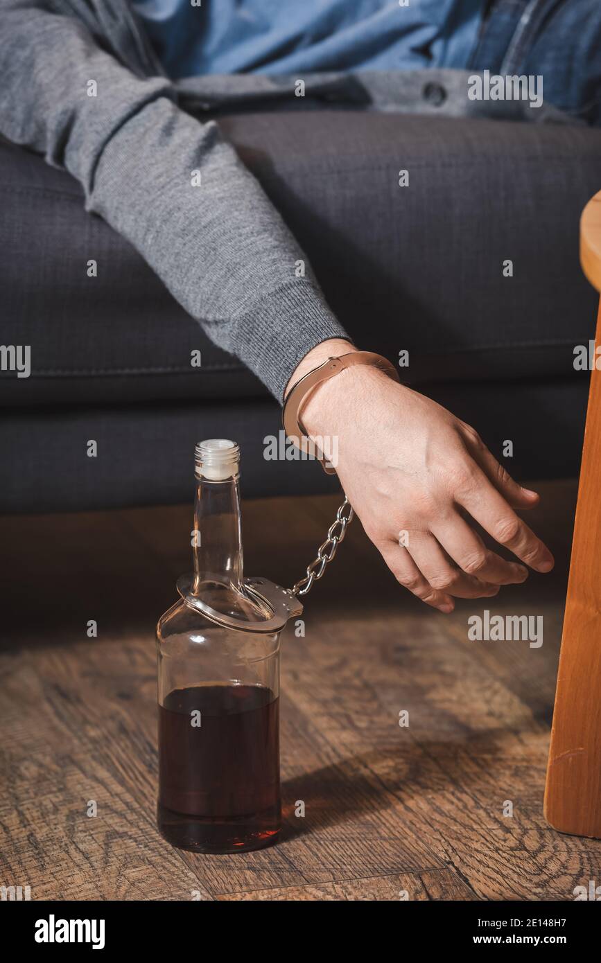 cropped view of drunk, sleeping man, handcuffed to bottle of whiskey Stock Photo