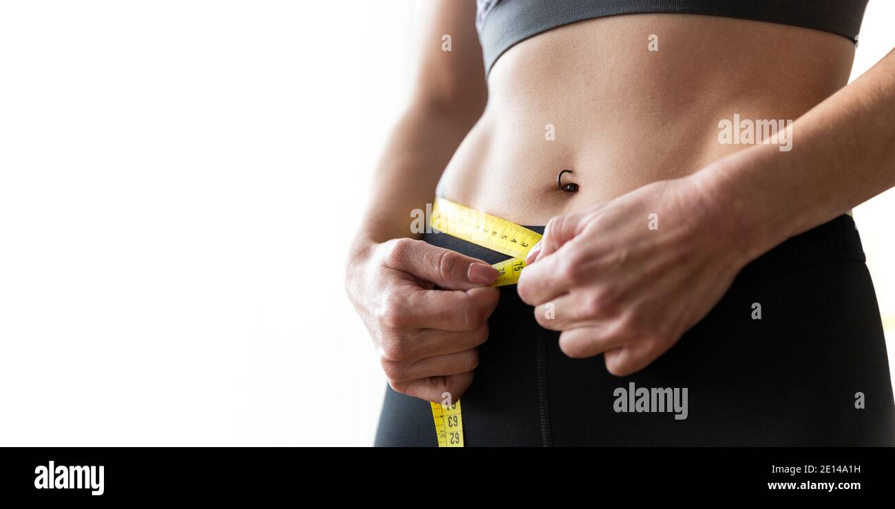 Close up of unrecognizable slim young woman measuring her waist with a tape measure. Concept of healthy lifestyle and weight loss. Space for text. Stock Photo