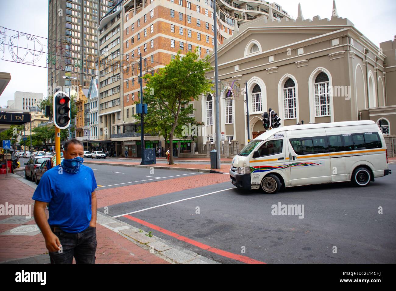 Cape Town, South Africa - 23/11/2020 Cloudy day in Cape Town. Man with wearing blue t-shirt and face-mask walking by. Taxi in background. Stock Photo