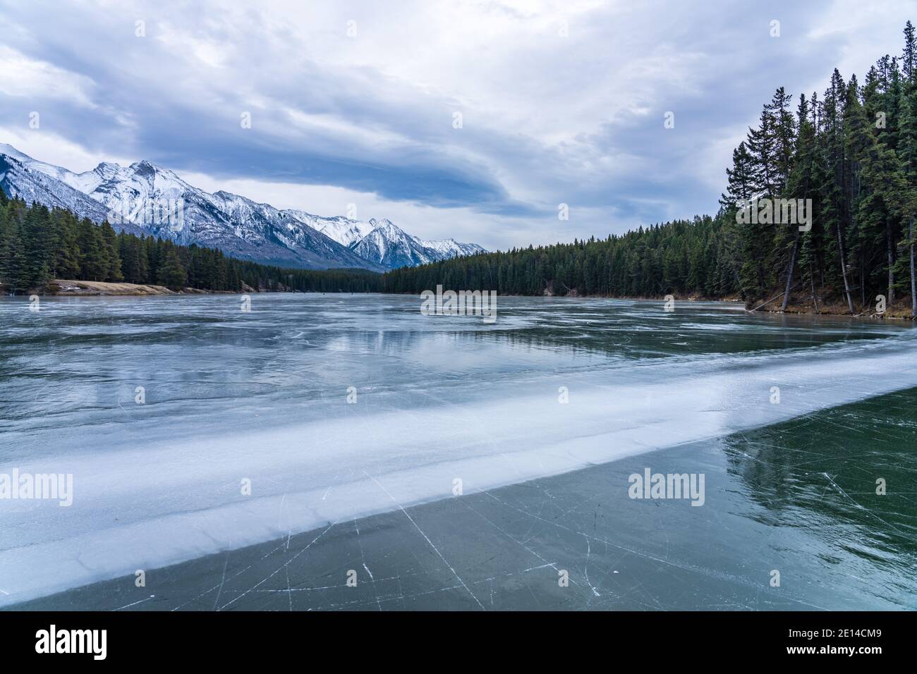 Johnson Lake frozen water surface in winter time. Snow-covered mountain in the background. Banff National Park, Canadian Rockies, Alberta, Canada. Stock Photo