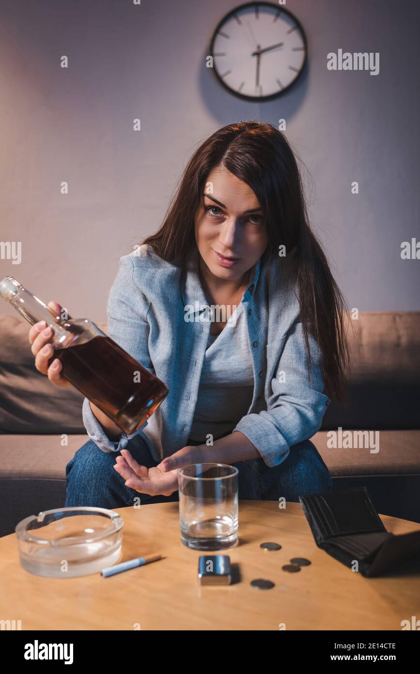 alcohol-addicted woman looking at camera while holding bottle of whiskey Stock Photo
