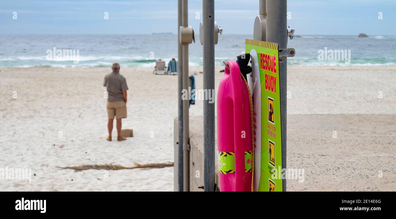Camps Bay-  Cape Town, South Africa - 23/11/2020 Colorful pink rescue buoy attached to a light green sign. Hanging on the metal showers of Camps Bay. Stock Photo