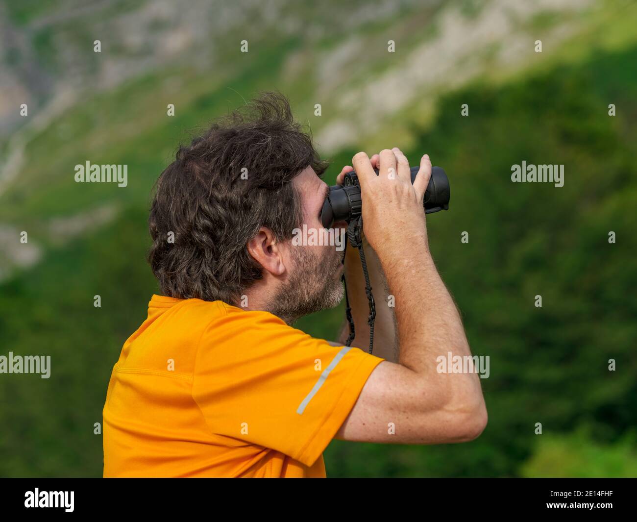 The hiker does bird watching with binoculars in the mountain nature park in search of birds of prey. Man scans the sky with binoculars. Stock Photo