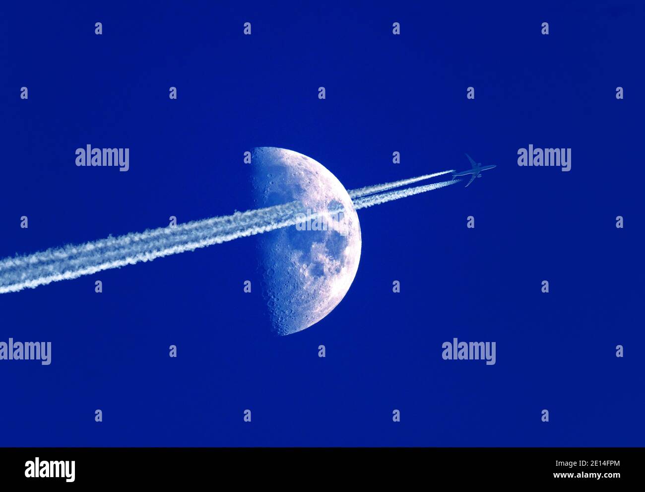 High flying jet aircraft with contrails passing in front of a half moon at dusk Stock Photo
