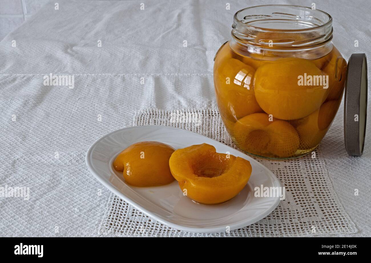 pesche sciroppate in vaso di vetro con piatto e tovaglia Stock Photo