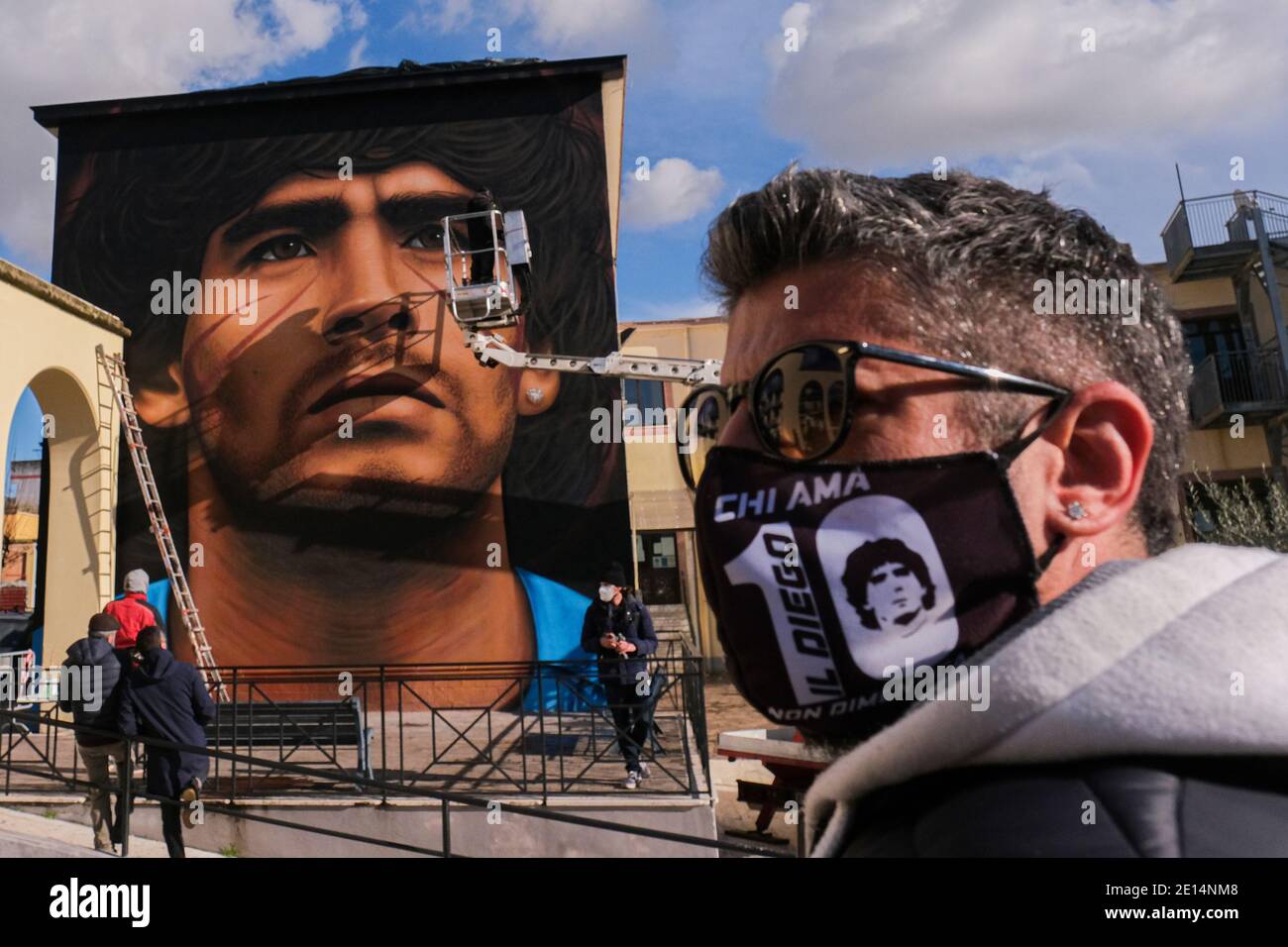 Luigi a local boy wears a mask to contain the infection from COVID- 19 depicting Maradona in the square to admire the new mural Jorit Agoch street artist from Naples, creates his new mural in quarto in the province of Naples the face of Diego Armando Maradona died on 25 November 2020, Dique Luj‡n, Argentina, former player of ssc napoli from 1984 to 1991. The figure of maradona in naples and the province is revered as a saint. Stock Photo