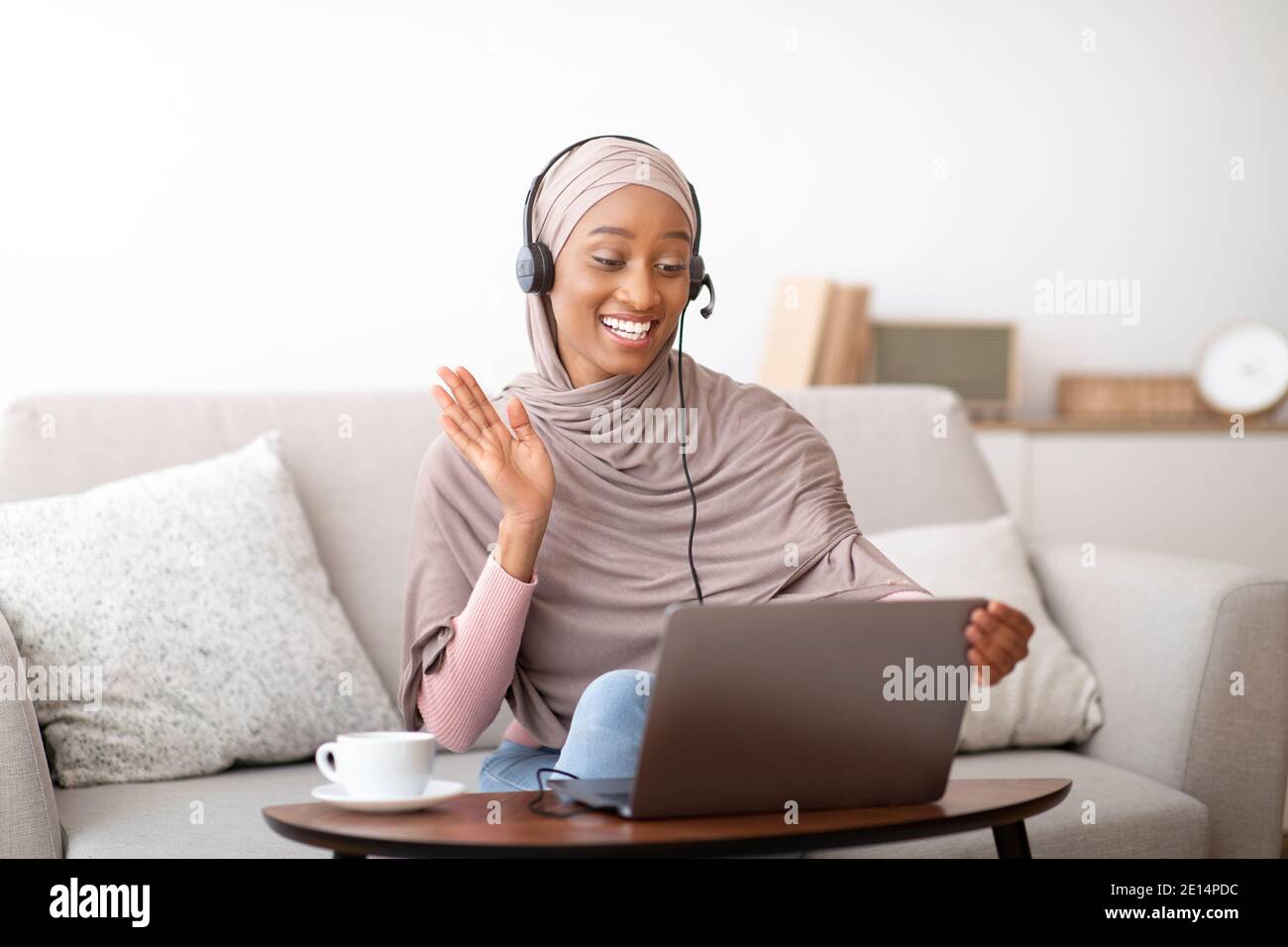 Happy black Muslim lady in hijab and headset making video call on ...