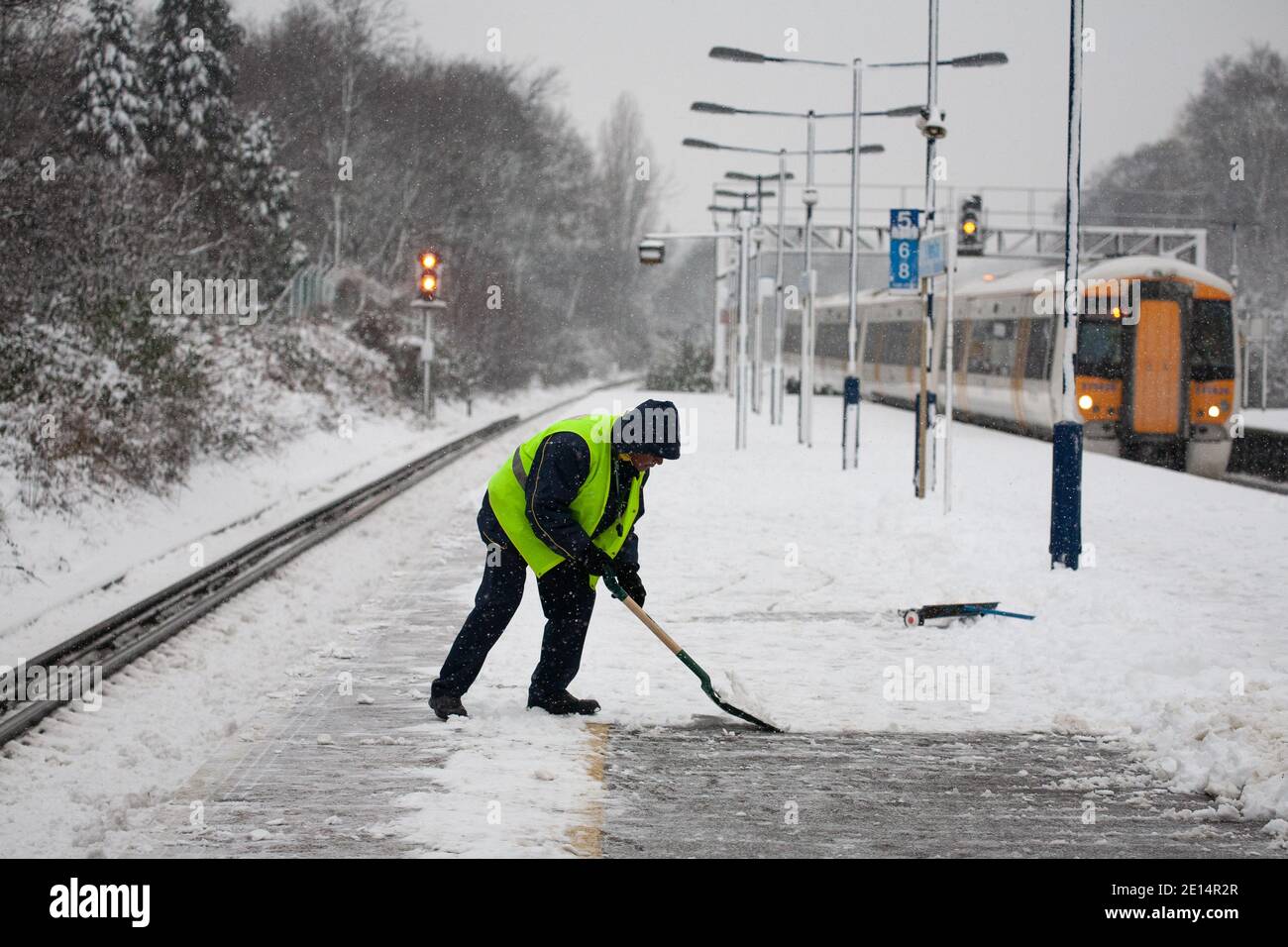 Station staff shovelling snow off Greater London mainline platform during the morning commute as a train arrives Stock Photo