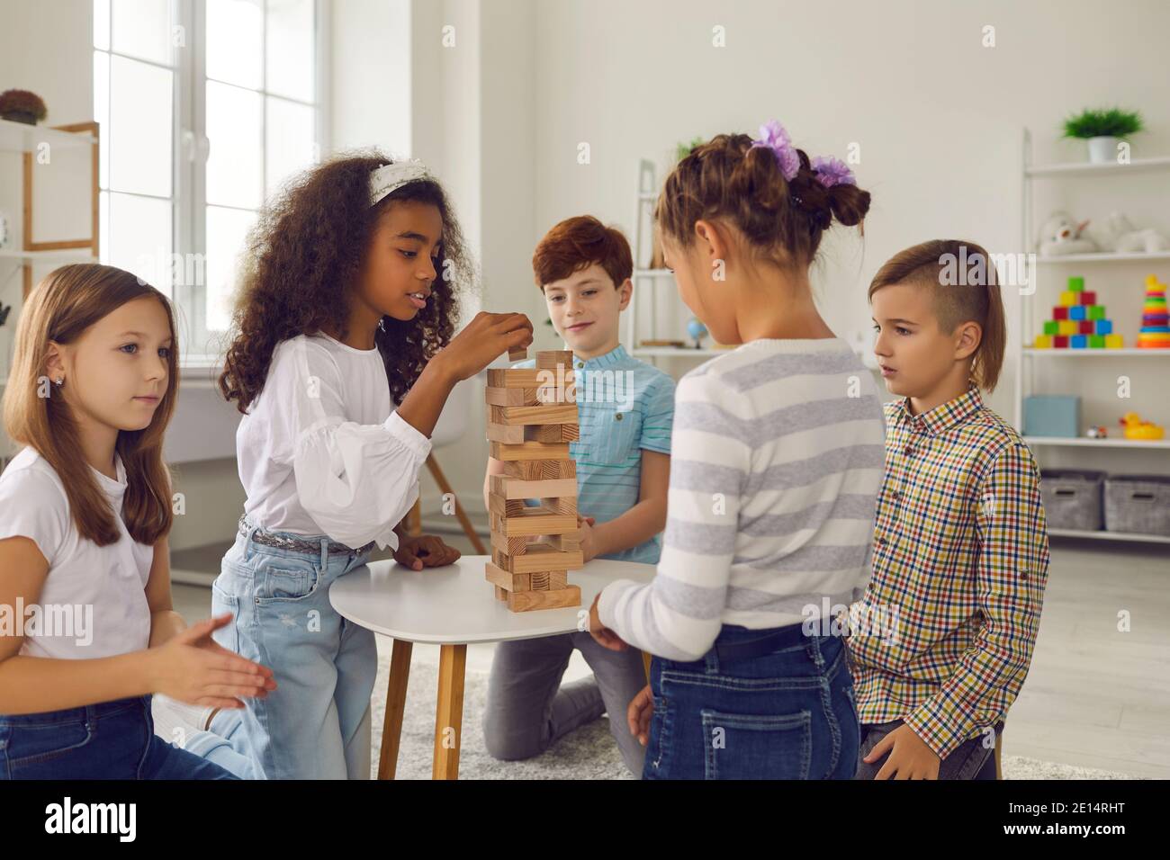 Group of mixed race children friends playing with building wooden pyramid together at home Stock Photo